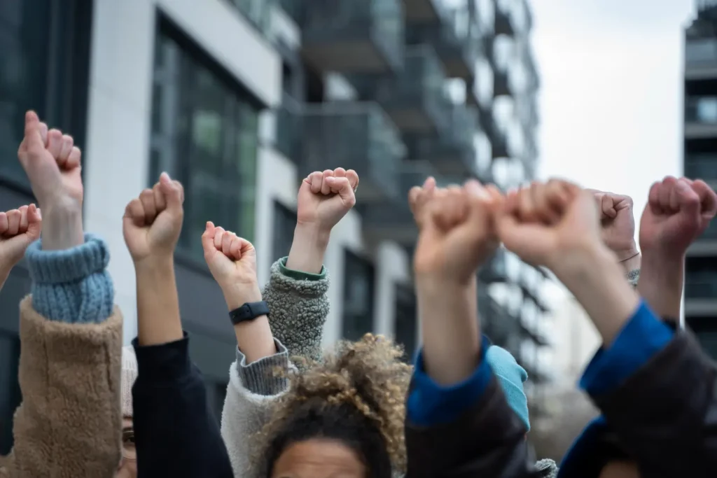 Pessoas com o punho cerrado para o alto em um protesto. Texto sobre contribuição sindical.