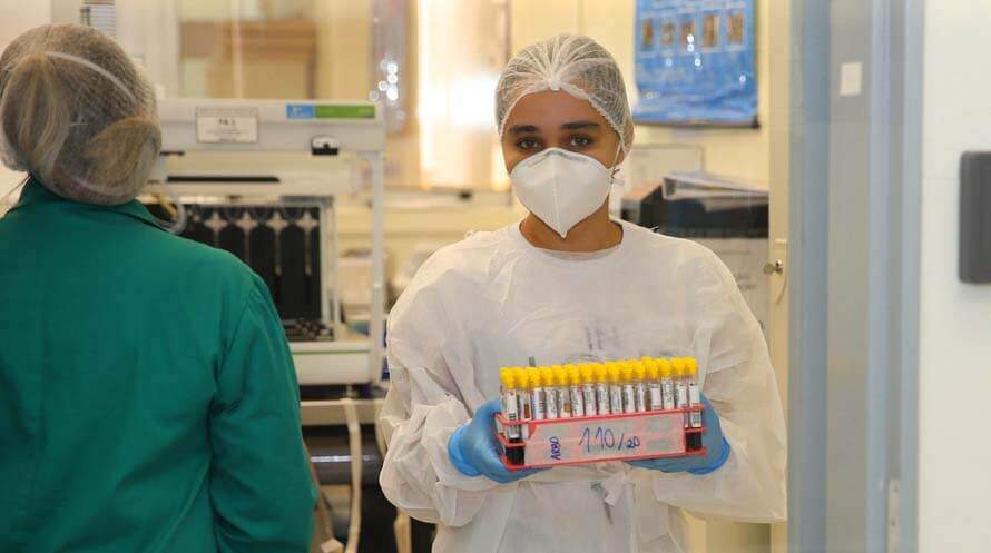 Na imagem, mulher com roupas de proteção em laboratório de testes de coronavírus. Conteúdo sobre "economia de guerra"