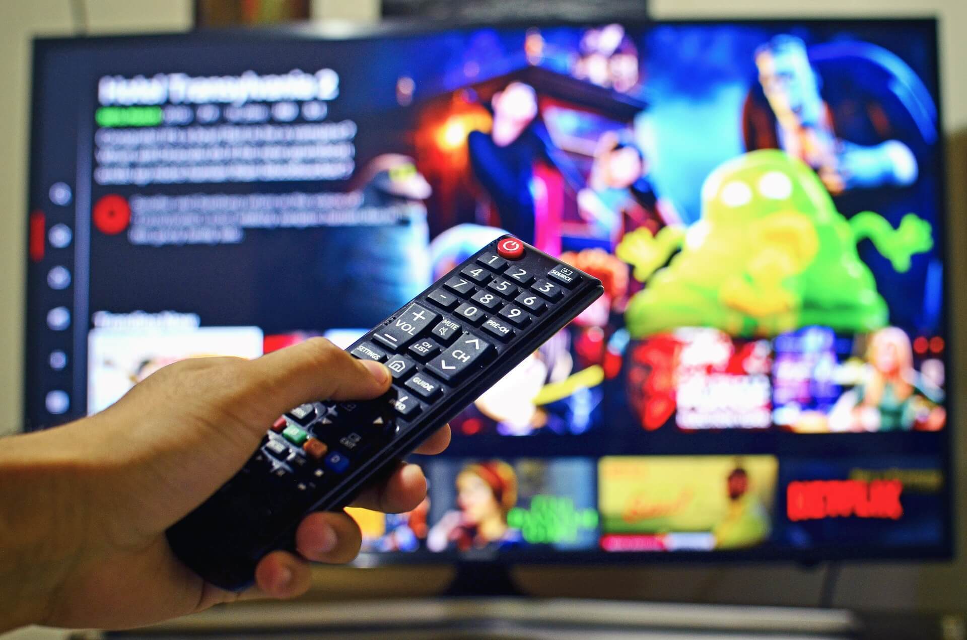 Na imagem, uma mão segurando um controle remoto apontando para a TV. Conteúdo sobre "5 séries sobre política"