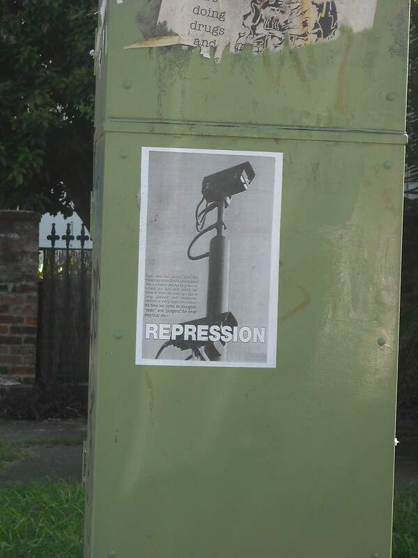 Na imagem, um cartaz escrito Repression com a figura de uma camera de vigilância. Conteúdo sobre as principais violações de direitos humanos.