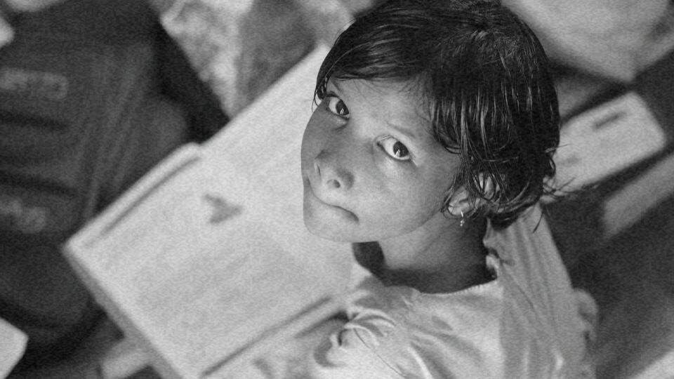 Imagem de uma criança estudando com um livro aberto e olhando para a foto, representando os direitos das crianças protegidos pelo Conselho Tutelar