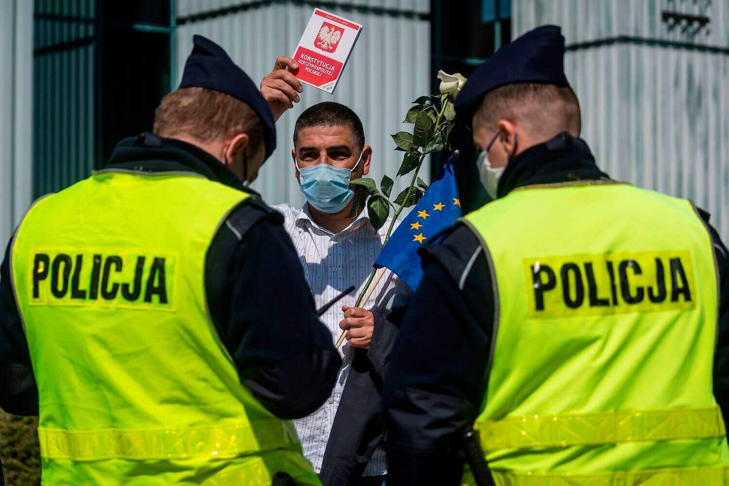 Um homem possui uma cópia da Constituição polonesa enquanto policiais checam sua carteira de identidade depois de participar de um protesto em Varsóvia, na Polônia, em 30 de abril. WOJTEK RADWANSKI / AFP via Getty Images