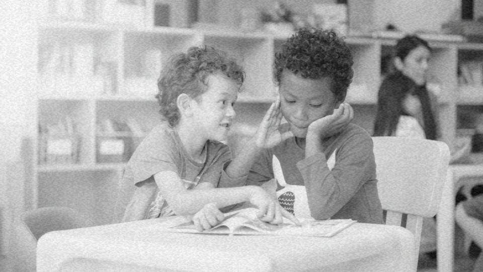 Imagem de duas crianças sentados à mesa rindo e aprendendo em uma escola, representando o direito à educação infantil e a construção da cidadania