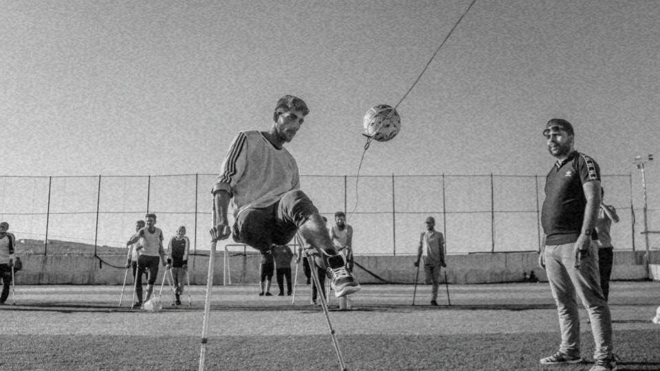 Imagem de um menino com deficiência física jogando futebol junto com outras pessoas