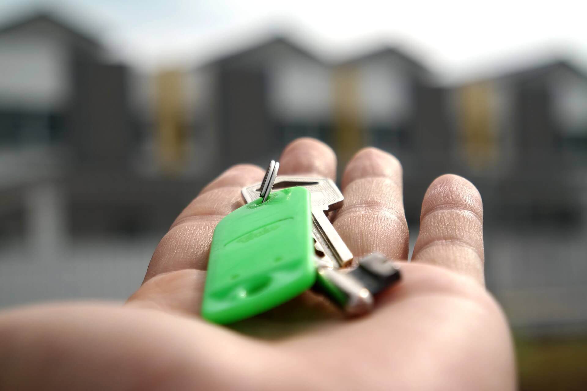 Outstretched hand with a key to a property, plus a green key ring |  Property right – Article Five