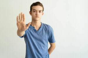 Jovem branco, de camiseta azul, fazendo sinal de "pare" com sua mão direita| Dissolução de associações – Artigo Quinto