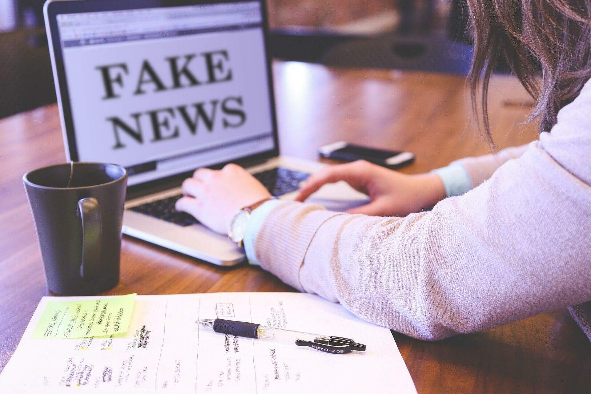 Na imagem, pessoa em frente ao computador onde mostra a imagem de fake news. Conteúdo Lei das Fake News.