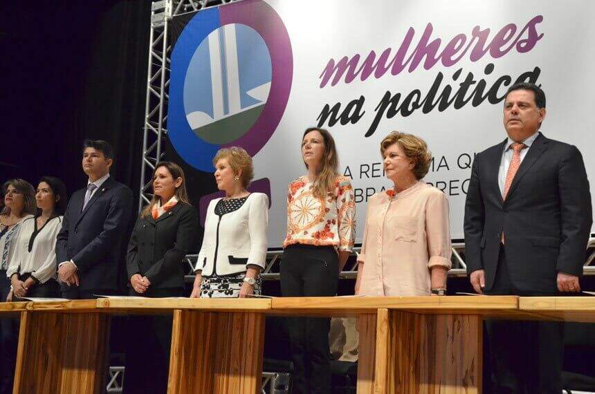 Na imagem, mulheres de pé ao redor de mesa. Conteúdo cotas de gênero nas eleições proporcionais.