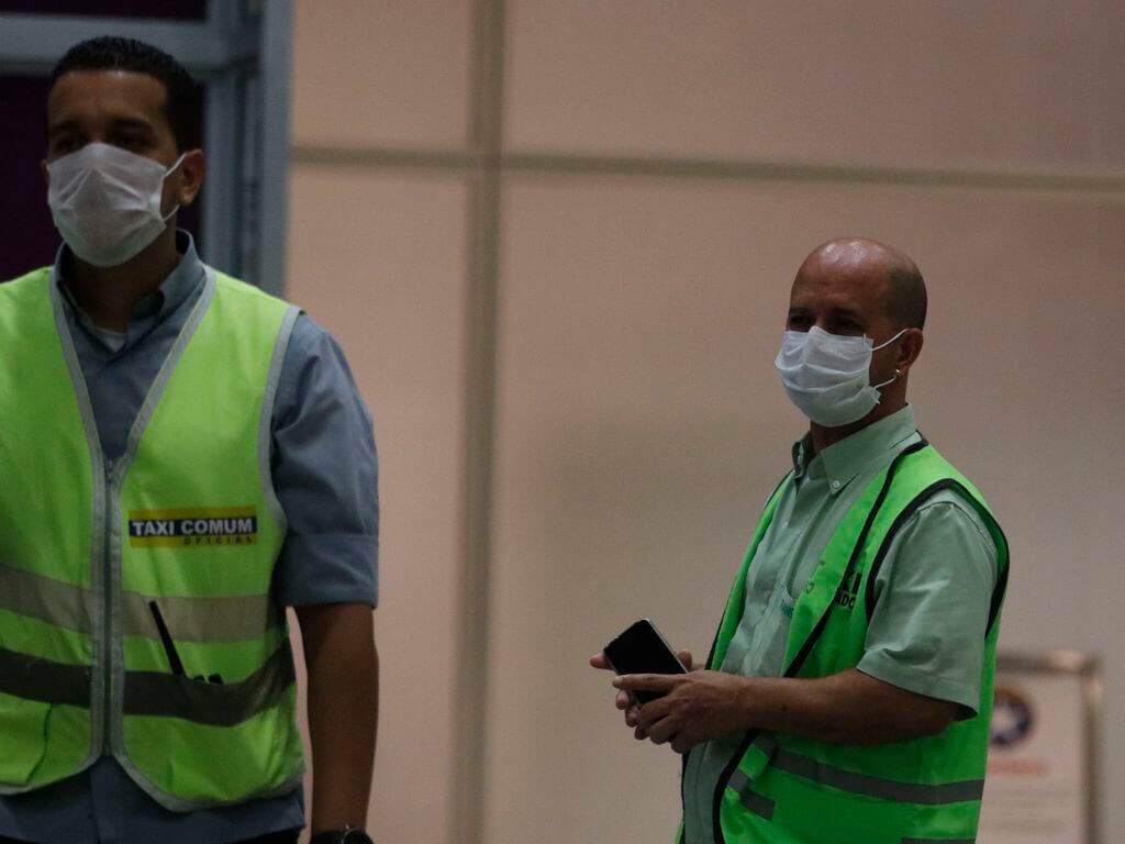 Funcionários do aeroporto com máscaras de cirurgia. Conteúdo sobre Estado de Emergência.