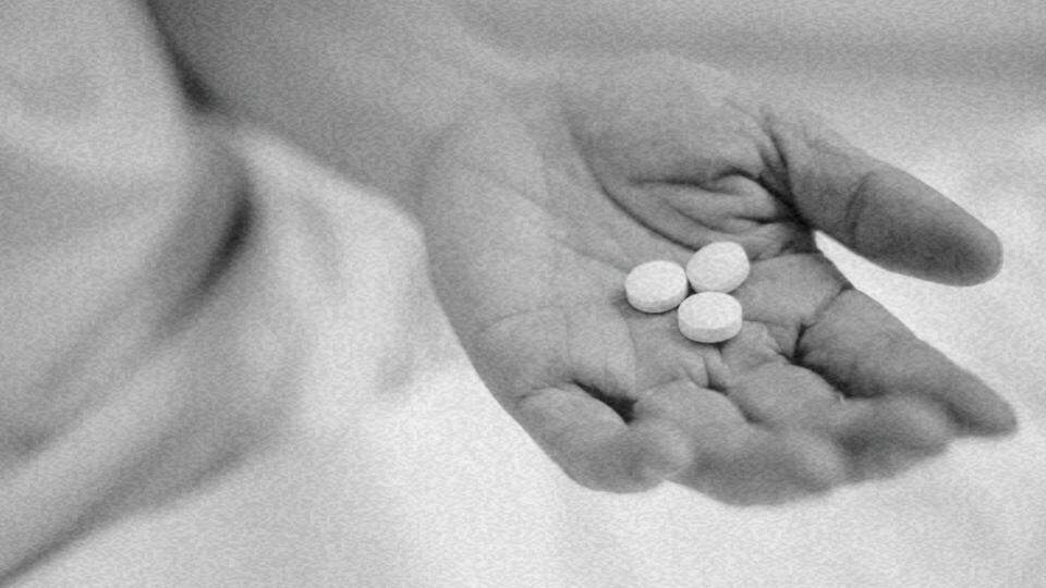 Imagem da mão de uma pessoa segurando três comprimidos de remédios representando o desafio do direito à saúde dos migrantes e refugiados