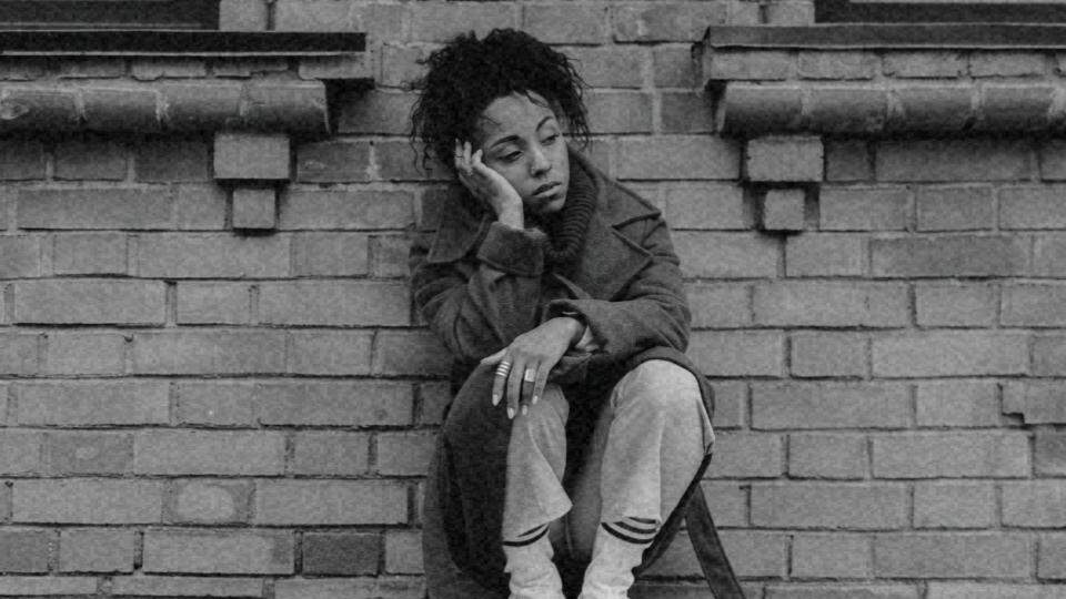 Imagem de uma mulher negra sentada na rua representando o racismo estrutural