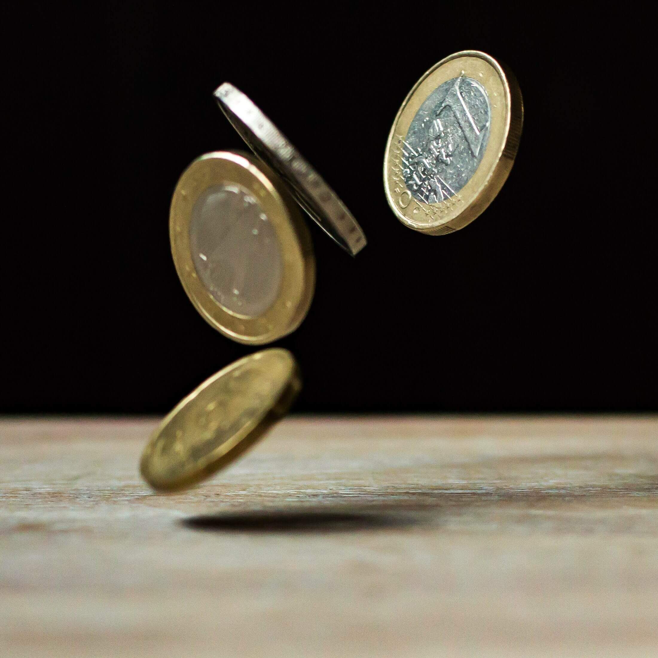 Na imagem, moedas caindo sobre mesa. Conteúdo sobre dividendos.