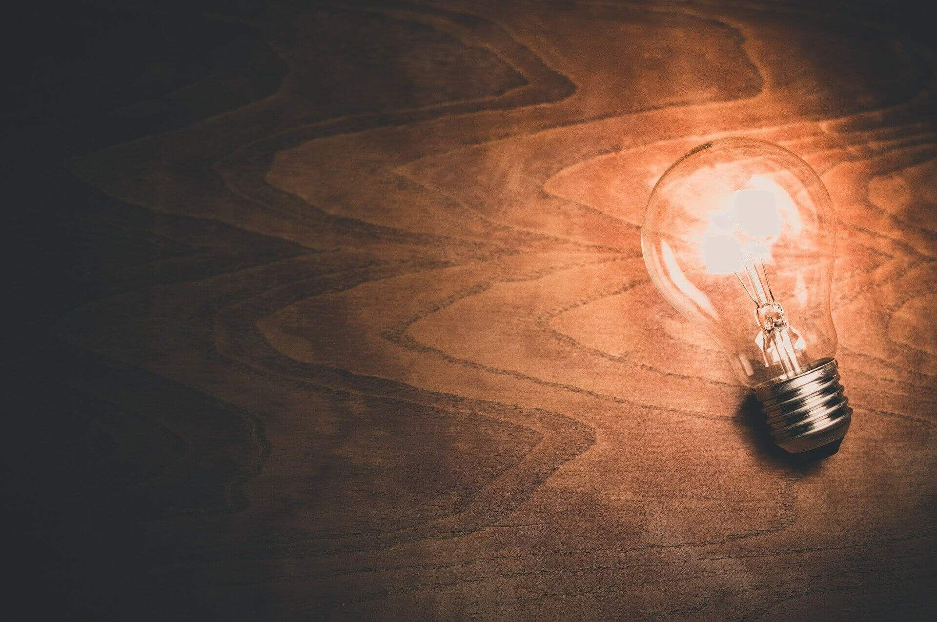 À direita, uma lâmpada acesa em uma mesa de madeira, representando o conceito de ideia | Propriedade industrial – Artigo Quinto