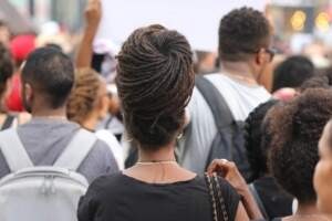 Pessoas de costas, em sua maioria, negras, protestando. Ao centro, uma mulher de tranças em formato de coque | Liberdade de reunião – Artigo Quinto