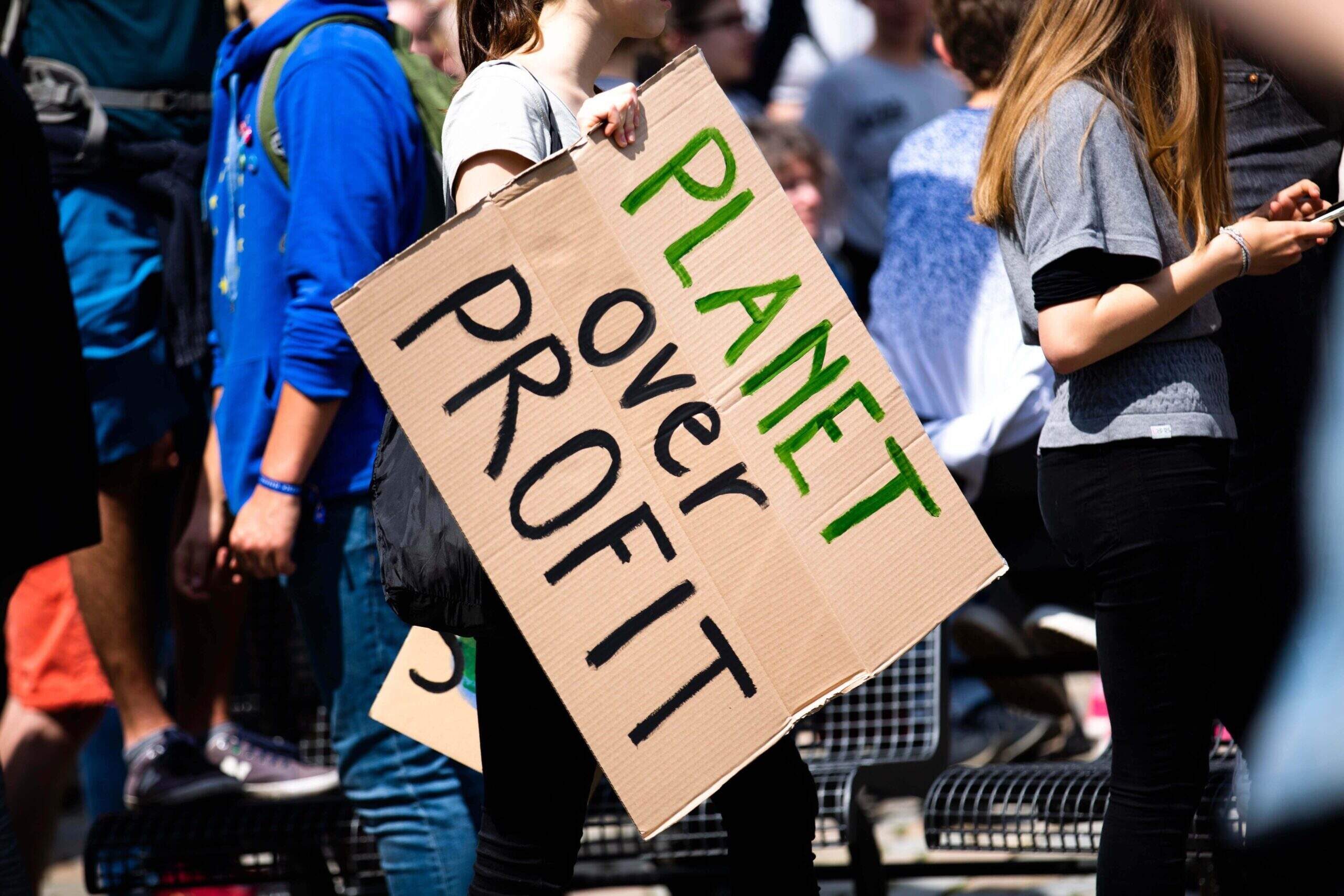 Na imagem, uma mulher segurando uma placa "planet over profit" durante manifestação. Conteúdo sobre ativismo empresarial.