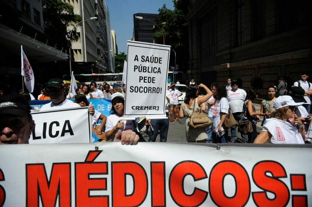 Pessoas em protestos pela saúde segurando ma placa "a saúde pública pede socorro". Conteúdo sobre Judicialização da saúde no Brasil.