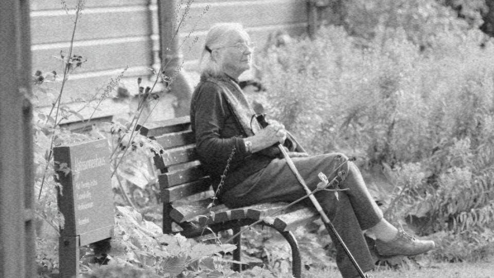 Imagem de uma mulher idosa sentada sozinha em um banco de uma praça representando o etarismo e o que ele representa aos idosos