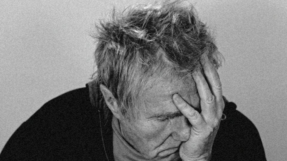 Imagem de um homem idoso com a mão no rosto e feição triste representando o etarismo e o que ele representa aos idosos