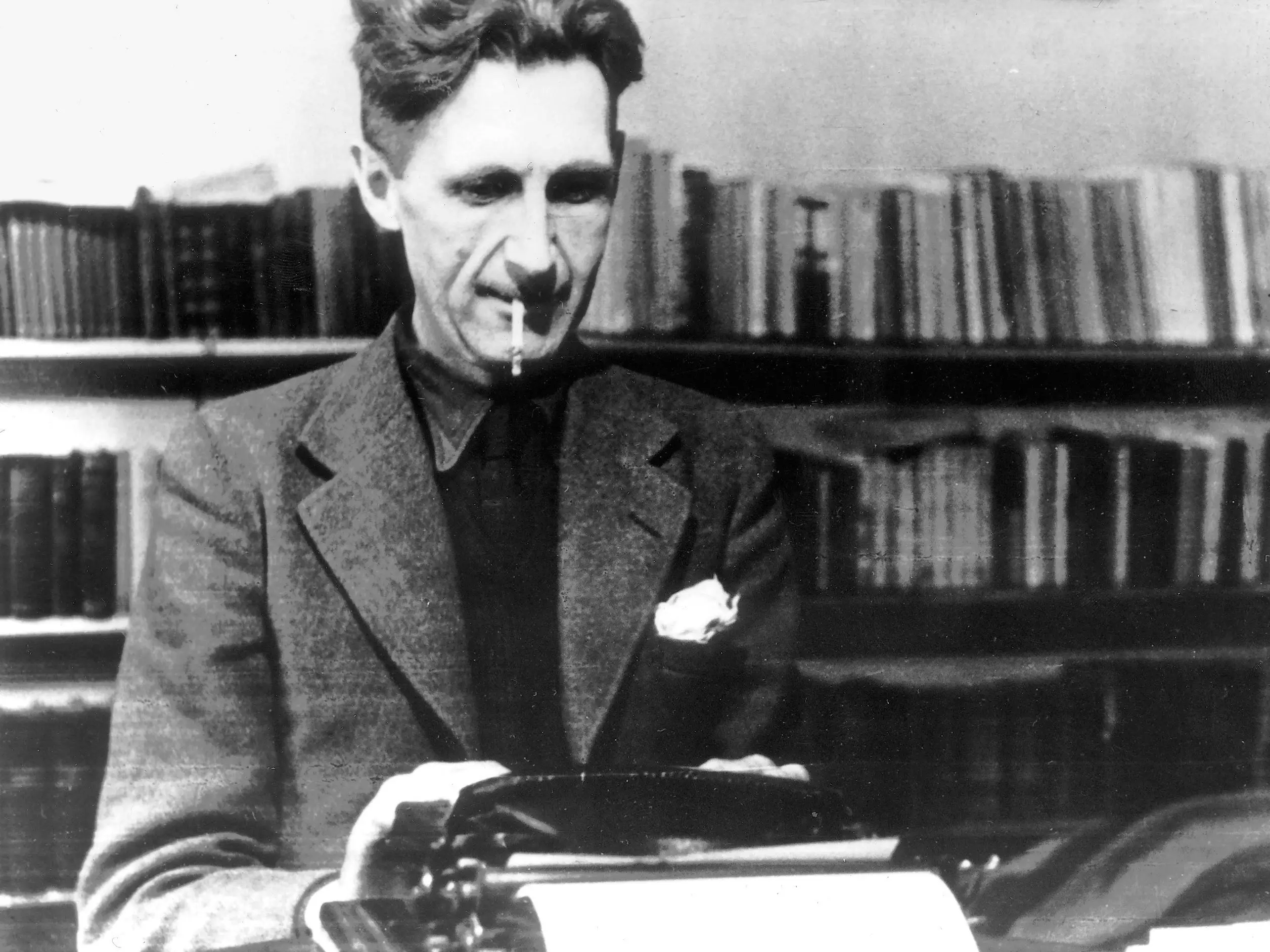 Homem branco, George Orwell, vestindo um terno, escrevendo em uma máquina de escrever com um cigarro na boca