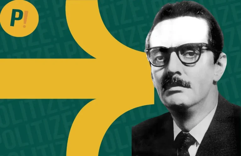 Homem sério, de bigode curto, óculos quadrado e terno, mas na imagem aparece apenas do seu busto para cima.