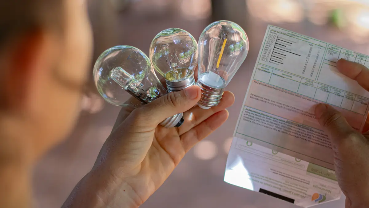 Pessoa segurando três lâmpadas de luz e uma conta de energia. Texto: Saiba tudo sobre a tarifa social de energia elétrica.