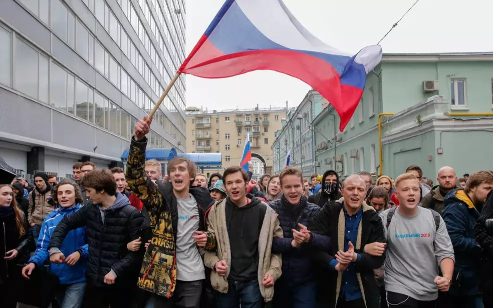 Manifestantes jovens nas ruas de Moscou, Rússia, com diversas bandeiras do país na imagem.