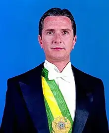 Imagem de fernando collor mais jovem usando a faixa presidencial, em um fundo azul.