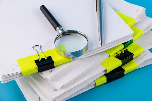 Lupa e caneta esferográfica sobre pilha de documentos. Texto sobre reforma administrativa.