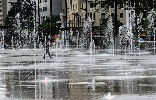Pessoa andando no meio de chafariz urbano, utilizado para minimizar o calor. Texto: O que são ondas de calor?