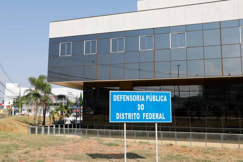 Fachada do prédio da Defensoria Pública do DF, com vidros espelhados e placa azul de identificação do local.